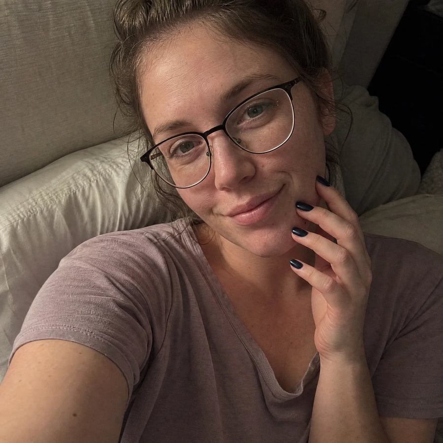 Candid nail-night campaign selfie showing a deep navy manicure in soft bedroom light.